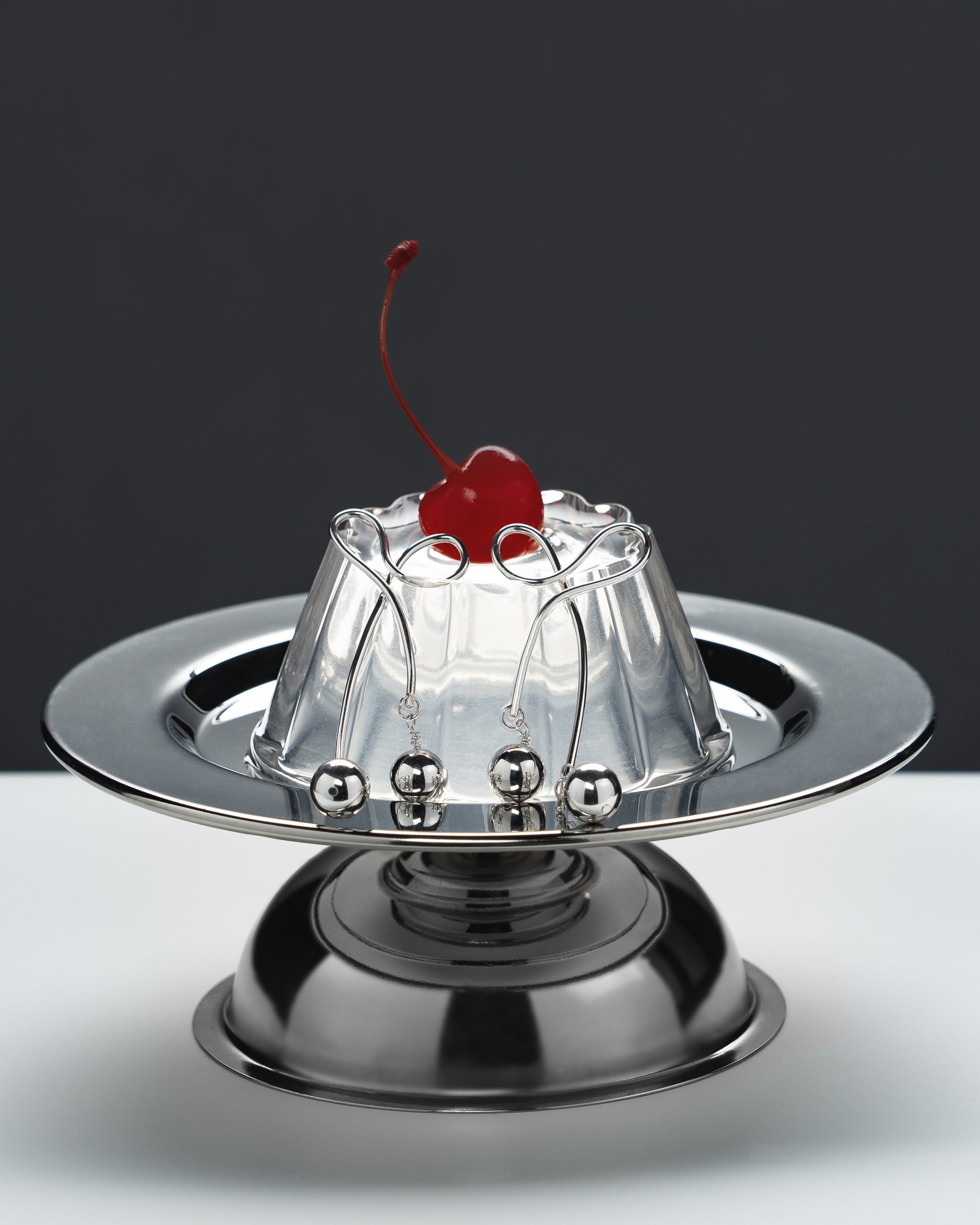 Silver cherry earring on top of a pudding