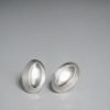Elongated oval stud earring in polished silver, featuring an off-center tilted 'thumb dent' mimicking the tactile response buttons of vintage MP3 players.