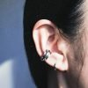 A small, chunky silver ear cuff with a rounded, convex profile. Designed to dock onto the ear cartilage without piercings, featuring a high-shine futuristic finish.