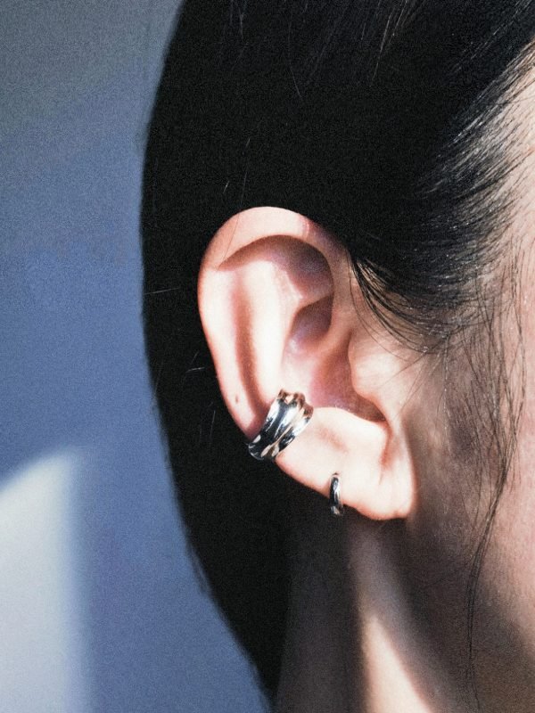 A small, chunky silver ear cuff with a rounded, convex profile. Designed to dock onto the ear cartilage without piercings, featuring a high-shine futuristic finish.